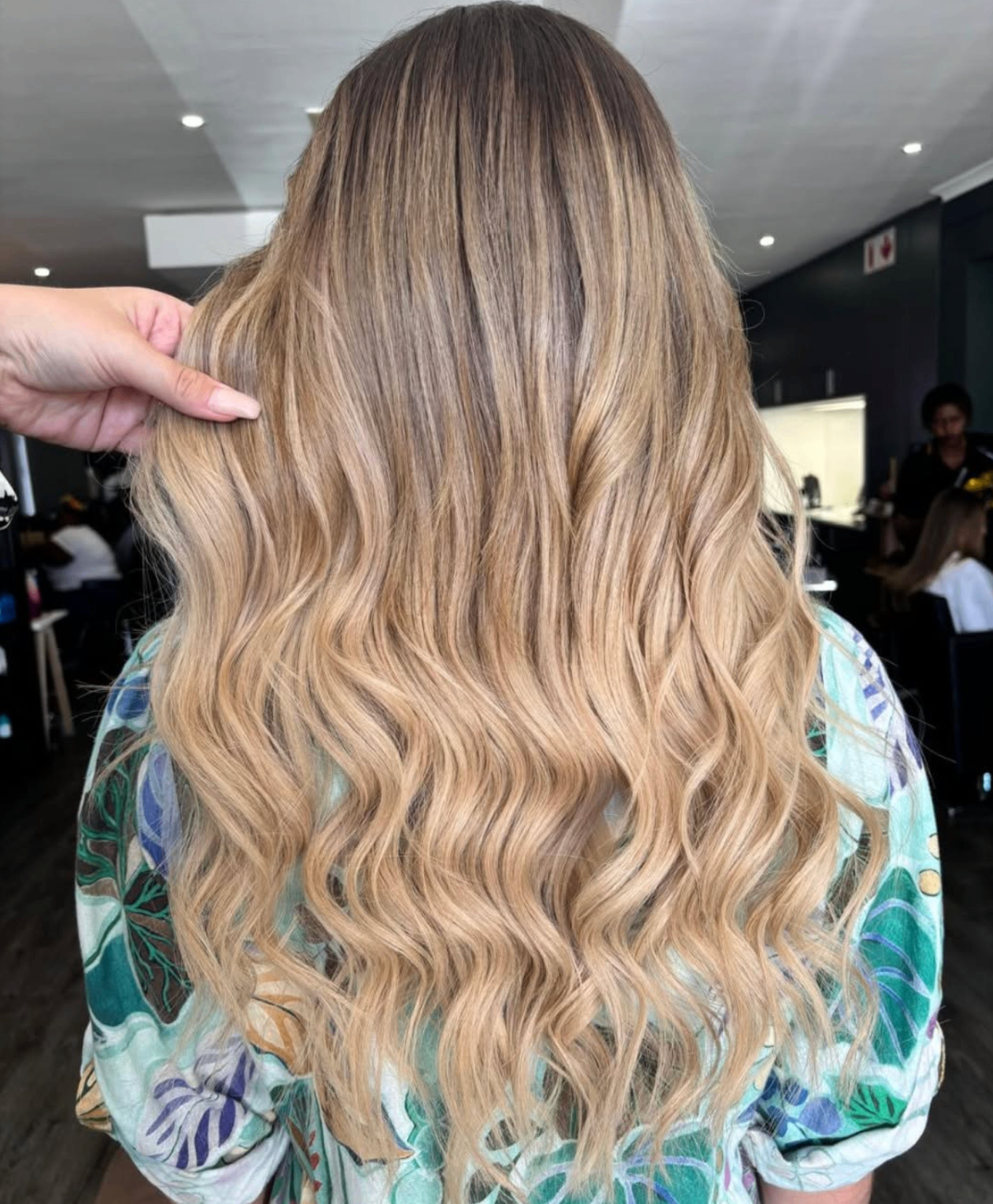 Long blonde balayage waves lifted by a stylist's hand at Liv Hair Studio